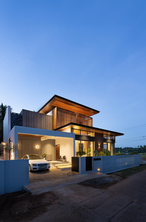 Modern two-storey home at dusk with a cantilevered timber-lined roof and lit carport